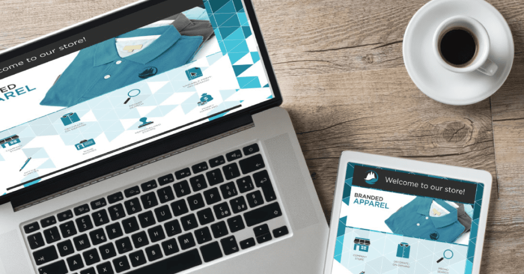 A laptop and tablet display the same online store homepage, showcasing a blue shirt. On a wooden table next to a cup of coffee, this setup reflects the streamlined efficiency akin to an ACES-supported dealership uniform program.